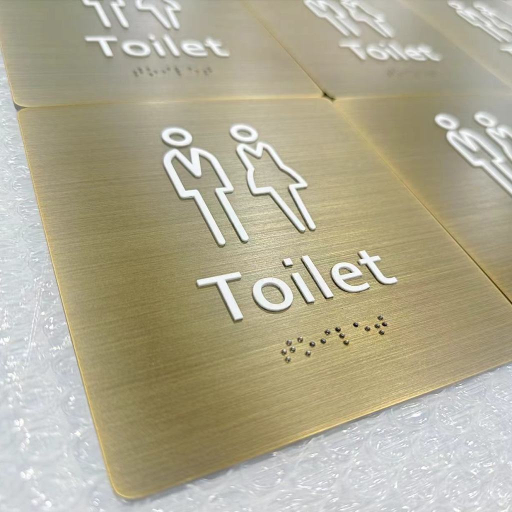 Alt : Plaque toilettes en laiton brossé avec pictogrammes et braille